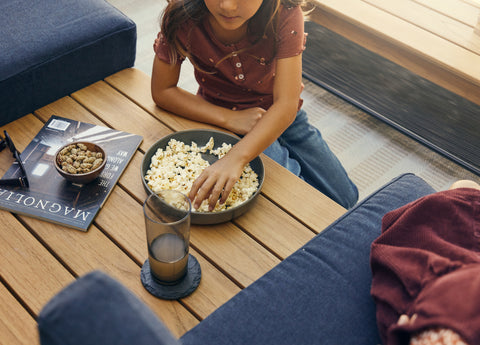 A young girl is eating a bowl of popcorn that's placed on in-line coffee table attached to an outdoor sofa
