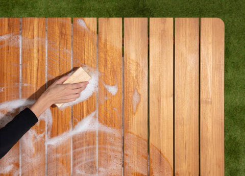 Woman scrubbing outdoor teak tabletop with soapy water